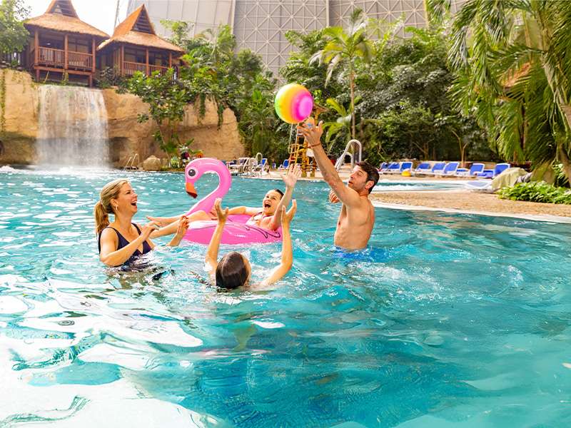 Family of 4 playing with a ball and an inflatable flamingo in the lagoon.