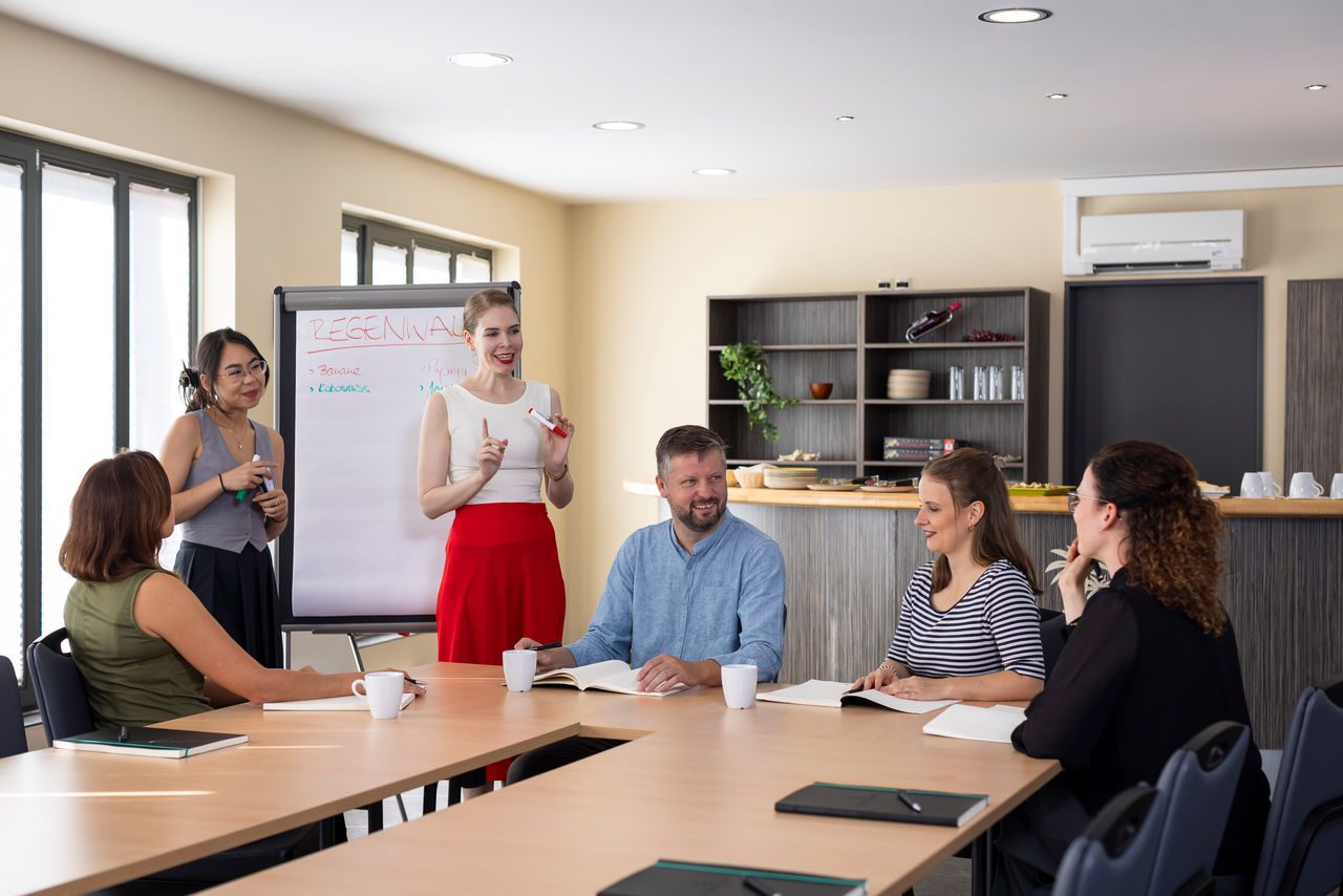 Sechs Kolleg*innen in lockerer Konversation im Seminarraum "Camp Club"