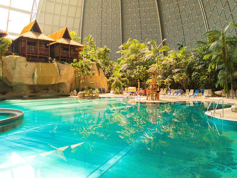 Indoor lagoon pool with tropical vegetation and the Waterfall Suites under a dome.