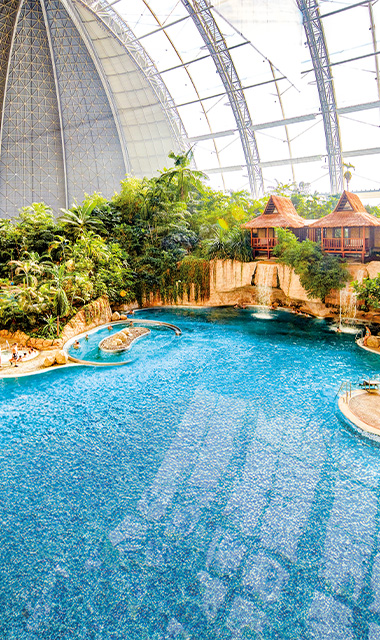 Indoor pool lagoon with tropical vegetation and the Waterfall Suites under a dome.