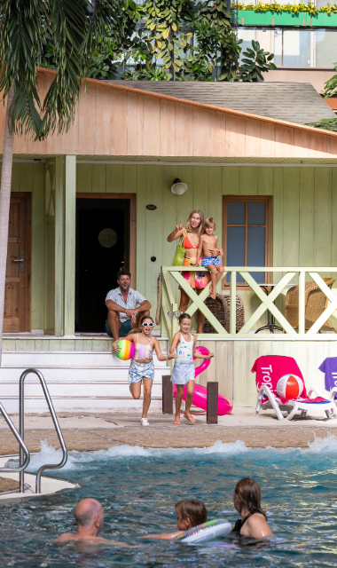 Familie mit Kindern steht auf der Terrasse eines grünen Hauses vor der Lagune.