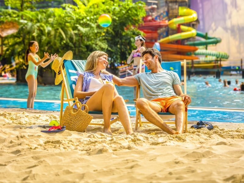 Sun loungers between palm trees in the Tropical Islands Dome, with the ‘South Sea’ pool and cloud panorama in the background