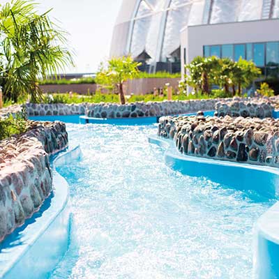 Ein geschwungener Wasserkanal mit Steinmauern und Palmen im Whitewater River.
