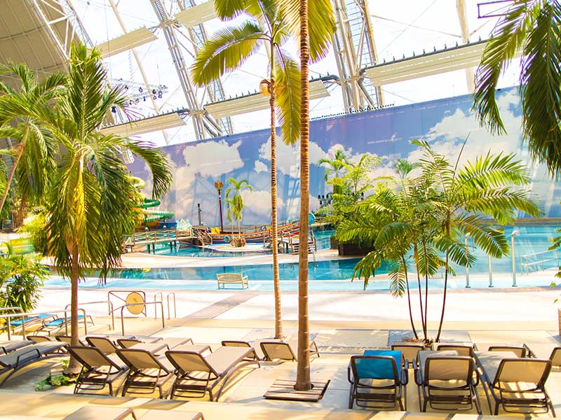 Tropischer Indoor-Poolbereich der Südsee mit Liegestühlen, Palmen und Sandstrand.