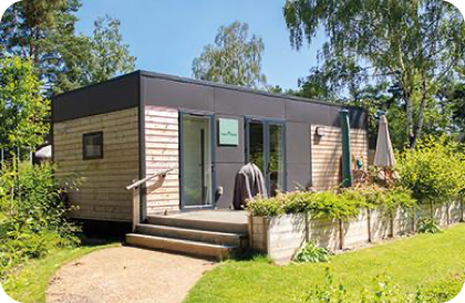  Modernes Woodland Home mit Holz- und Dunkelverkleidung, großen Glastüren und Terrasse mit Möbeln und Grill.