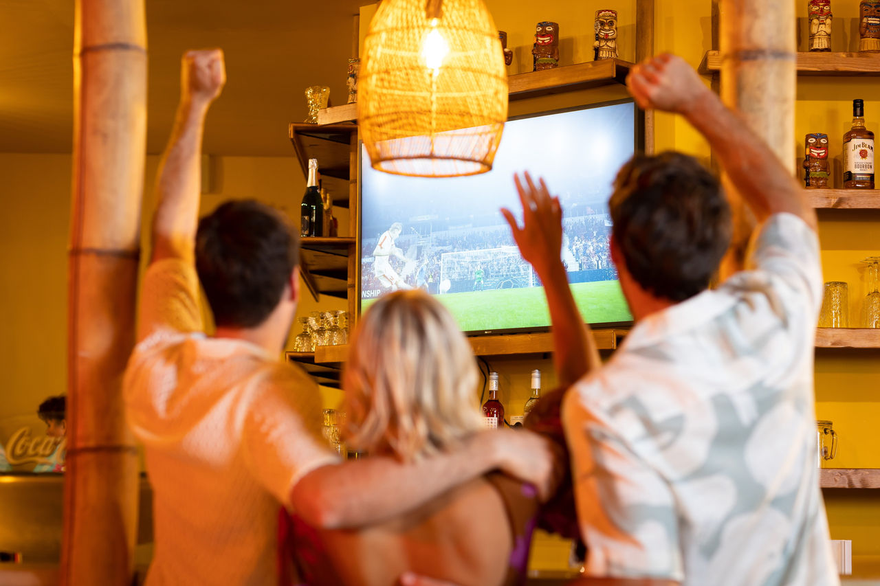 Guests at OHANA in Tropical Islands watching a football match together and raising their arms in front of big screens