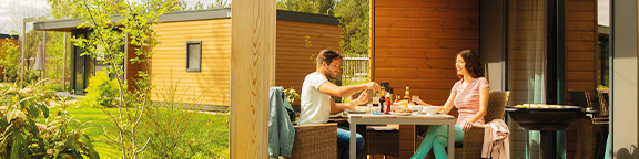 Zwei Personen essen auf der Terrasse eines modernen Nature Homes, umgeben von Pflanzen und Bäumen.