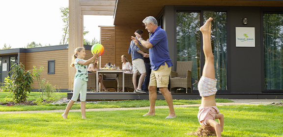 Ein Mann spielt mit Kindern vor einem Ferienhaus.