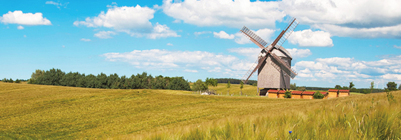 Eine traditionelle Windmühle steht auf einem weiten Feld unter blauem Himmel.