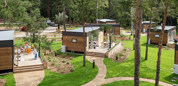 Mehrere moderne Woodland Homes mit großen Fenstern in einem bewaldeten, gepflegten Gartenbereich