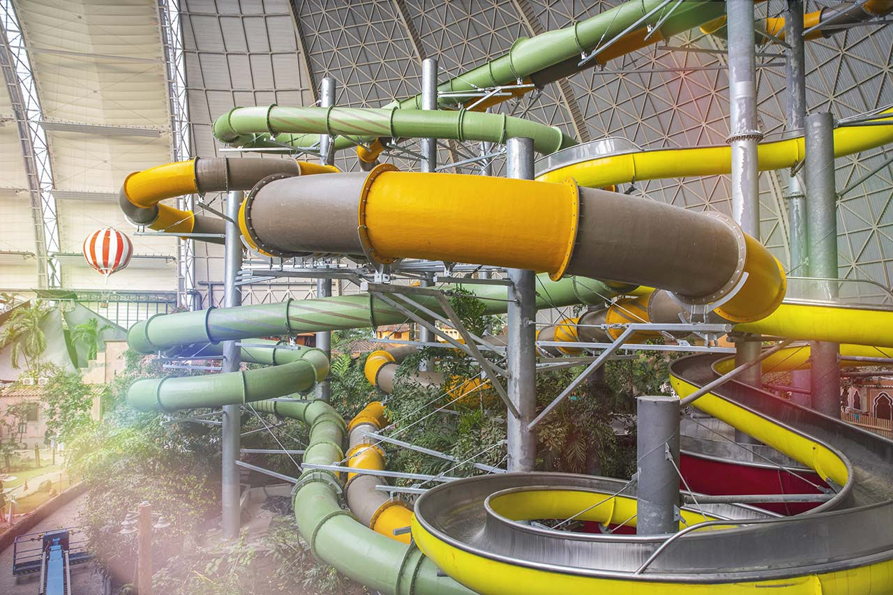 Wasserrutschen-Turm mit bunten Rutschen, umgeben von tropischer Bepflanzung und einem Ballon