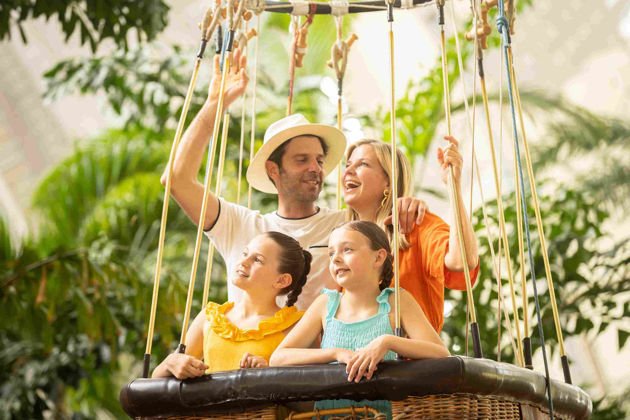 Familie mit Frau, Mann und zwei Mädchen steht im Ballon und freut sich.