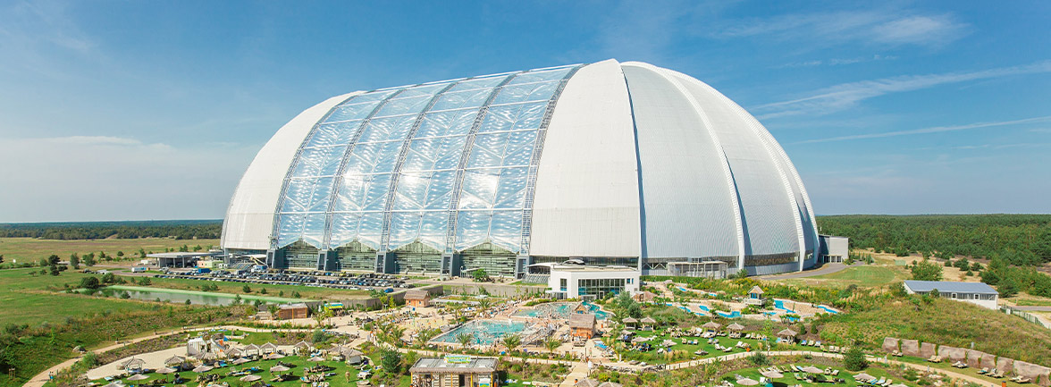 Liegewiese mit Sonnenliegen und Schirmen vor der großen Kuppel der Tropical Islands Halle