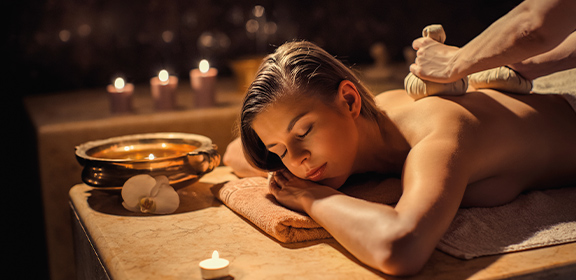 Eine Person liegt auf einer Massageliege, im Hintergrund stehen Kerzen und eine Schale.