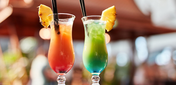Zwei bunte Cocktails mit Ananasscheiben und Strohhalmen stehen auf einem Tisch.
