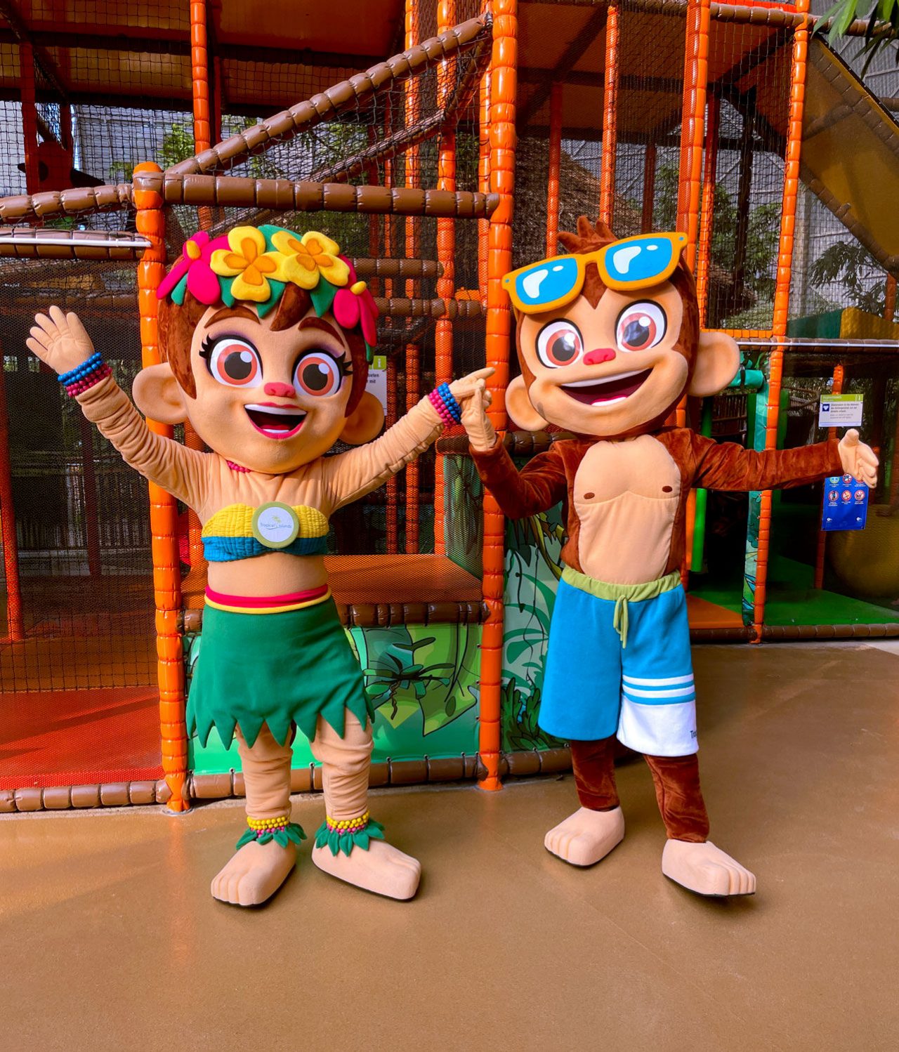Maskottchen Tiki & Isla in freudiger Pose vor dem Indoor_klettergerüst im Tropino Kinderclub