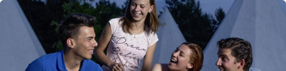 Vier Personen stehen im Freien vor Zelten oder Tipis auf dem Campingplatz.