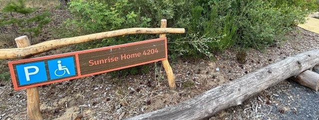 Holzgebäude mit barrierefreiem Parkplatzschild Sunrise Home 4204, umgeben von Grün und Kiesweg