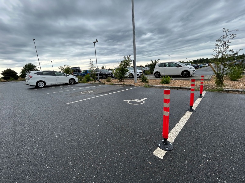 Parkplatz mit mehreren Autos, ausgewiesener Stellplatz für Menschen mit Behinderung mit Absperrpfosten
