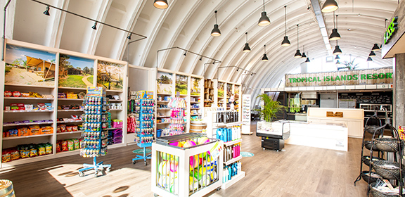 Ein heller Shop mit Bistrobereich bietet Snacks, Souvenirs und Postkarten unter einem geschwungenen Dach.