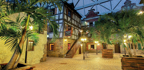 Die Hafenstadt Royal Harbour zeigt einen stimmungsvoll beleuchteten Platz mit Palmen, Fachwerkfassaden und Hafenflair.