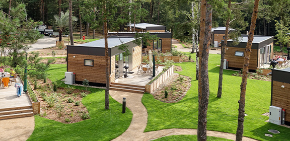 Mehrere moderne Woodland Homes mit großen Fenstern in einem bewaldeten, gepflegten Gartenbereich
