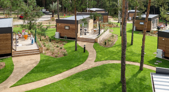 Überblick über den Woodland Homes Park mit grünem Rasen und Kiefern, auf einer Terrasse ist eine Familie zu sehen