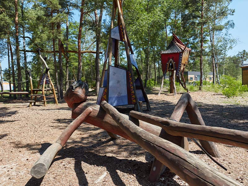 Niedrigseilgarten mit Holzskulpturen, darunter ein großes Insekt, sowie buntem Tipi und Stelzenhaus