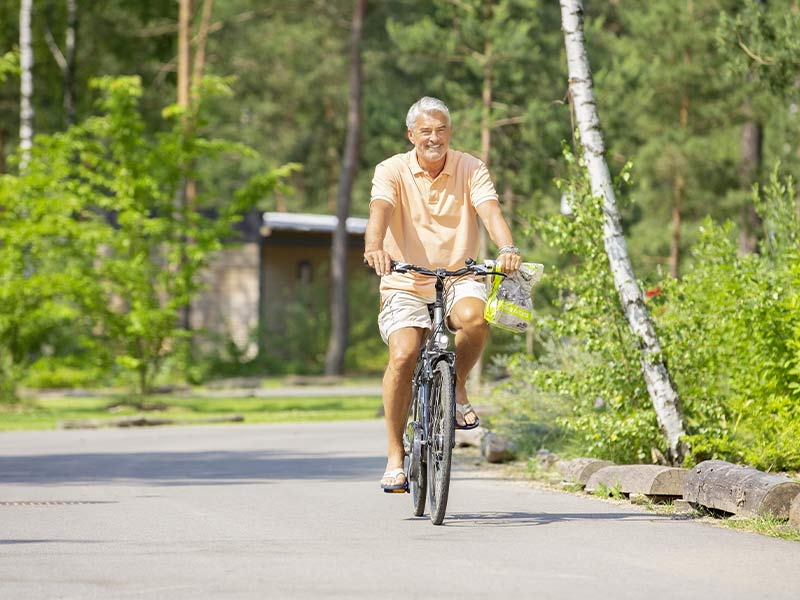 Person fährt Fahrrad auf einem Weg durch grüne, bewaldete Umgebung.