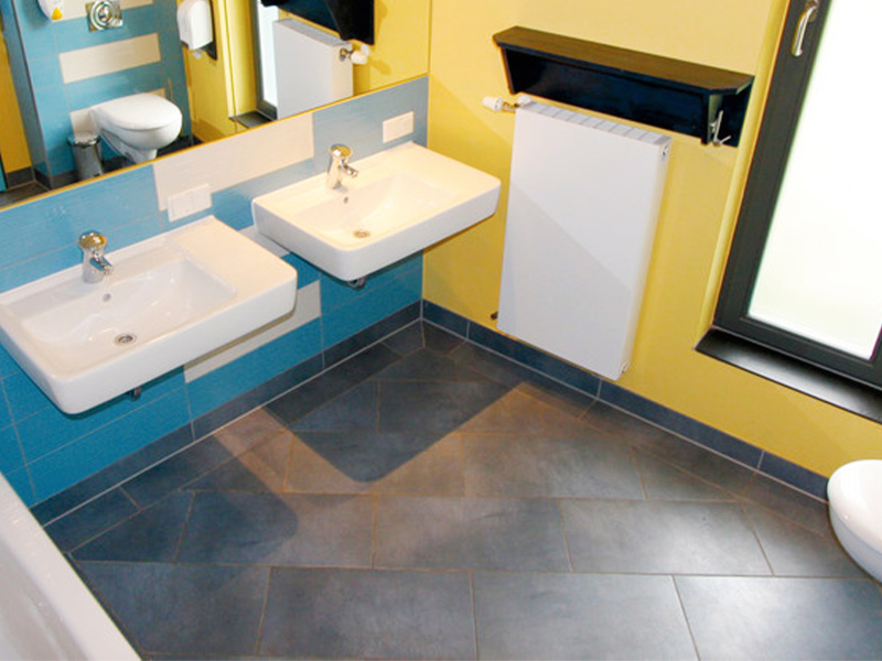 Badezimmer mit zwei weißen Waschbecken, Spiegeln, einem Fenster und einem Heizkörper.