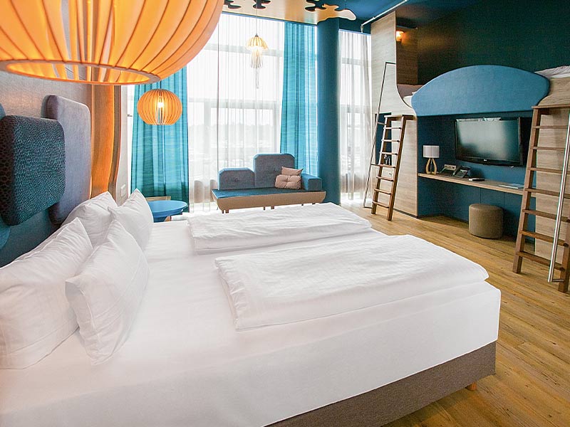 Modernes Hotelzimmer mit einem Doppelbett, gelbem Lampen und blauen Akzenten.