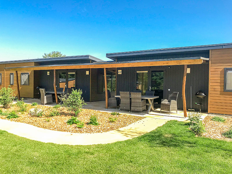 Modernes Sunrise Home Doppelhaus mit Holzfassade, großen Fenstern, überdachter Terrasse und Gartenweg.
