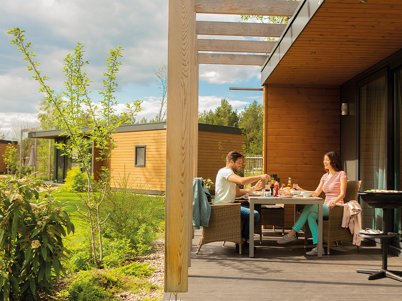 Zwei Personen essen auf der Terrasse eines modernen Nature Homes, umgeben von Pflanzen und Bäumen.