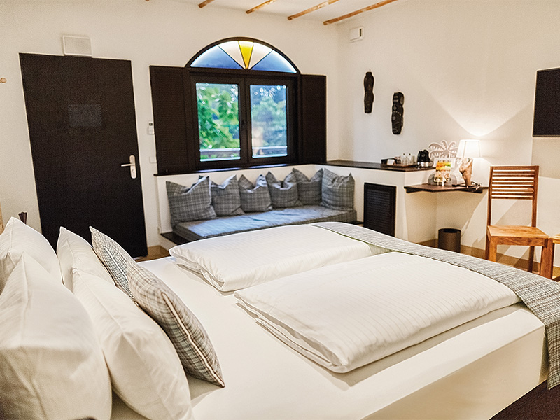 Modern eingerichtetes Schlafzimmer mit großem Bett, Sitzbereich am Fenster und Blick in die Tropen.