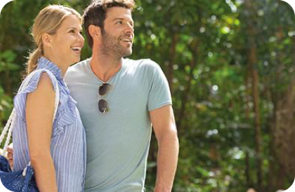 Two people in the rainforest, one in a striped shirt with a bag, the other in a green shirt with sunglasses.