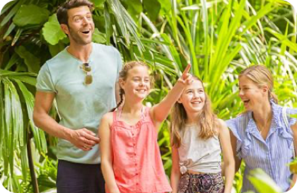  Four people in the rainforest—man in blue, woman in stripes, two kids, one pointing.