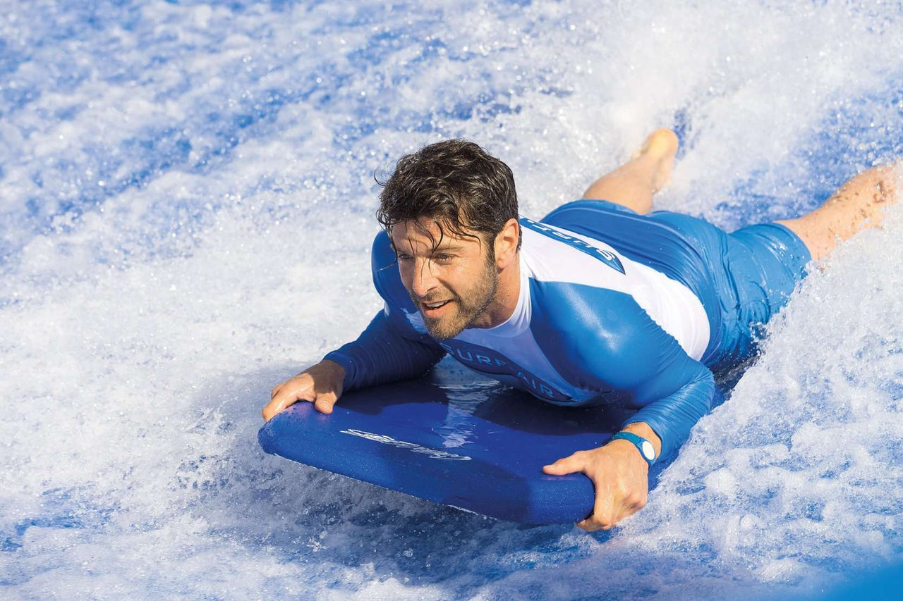 A person in a blue and white wetsuit lies on a bodyboard, gliding across the water.