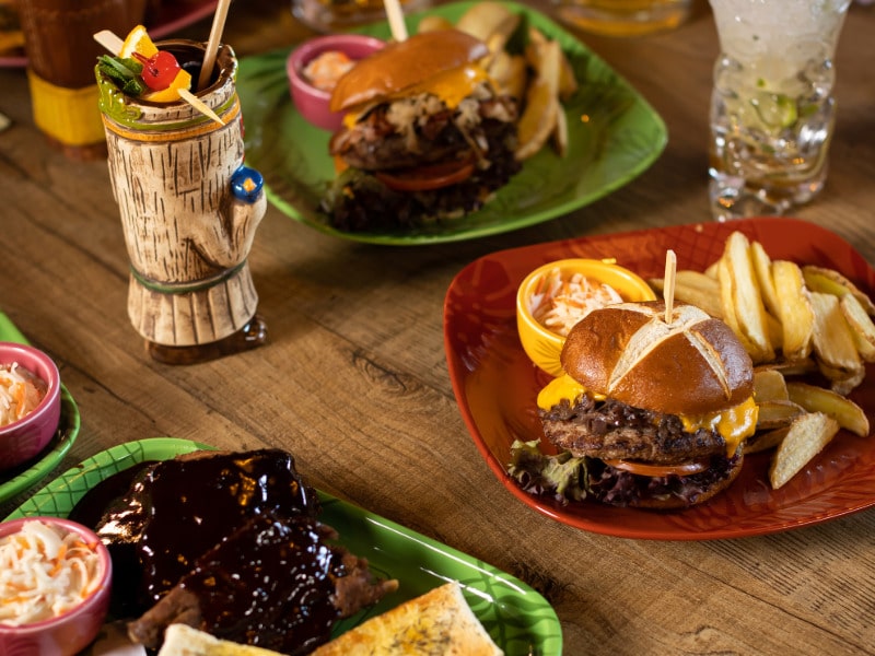 Table with burgers, ribs, other dishes and two drinks, colorfully arranged.