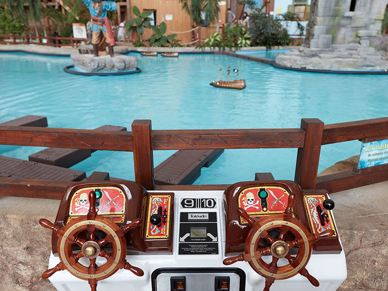 A water basin with small pirate boats, two steering wheels and a pirate figure in the background.