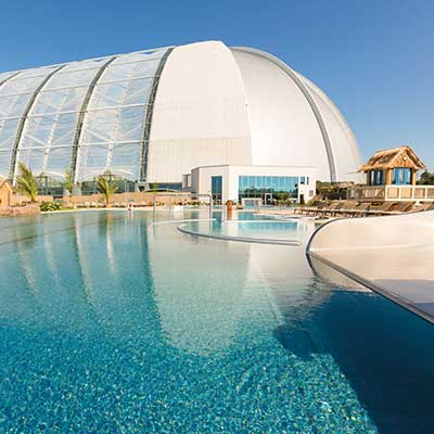 View of the outdoor pool at AMAZONIA with the striking white dome of Tropical Islands in the background under a blue sky.