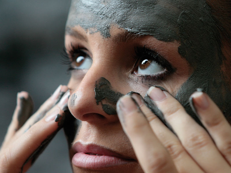 A woman applies a healing clay mask to her face.