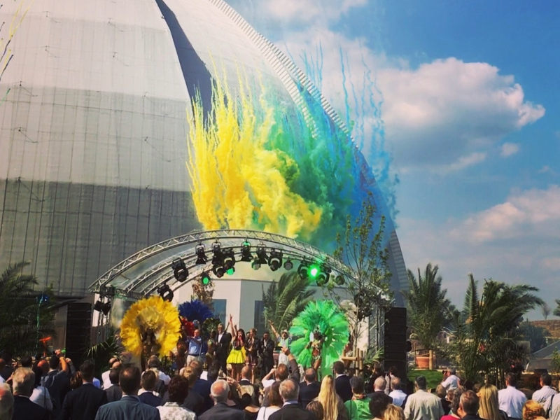 Outdoor event, yellow, green, and blue powder shoots into the air, with the hall in the background.