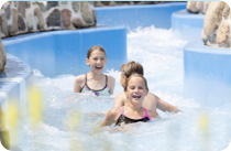 Three kids float in the Whitewater River current channel between blue walls and stone decorations.