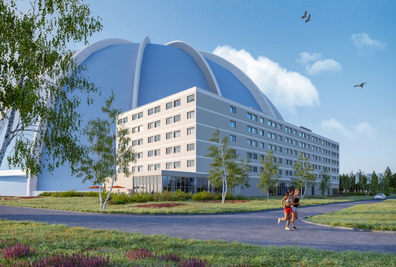 The Tropical Islands Dome rises behind the multi-story OHANA Hotel, surrounded by trees and a clear sky.