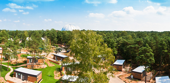 View over a forested area with small buildings and a large dome in the background under a partly cloudy sky.