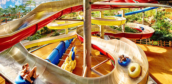 A colorful water slide tower with intertwined slides where visitors ride on tubes through a tropical setting.