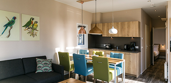 Wooden kitchen with black countertop, colorful dining area, and view of the living room and hallway in a nature home.