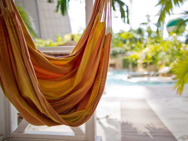 A fabric hammock hangs in the foreground, while a water pool and palm trees are visible in the background.