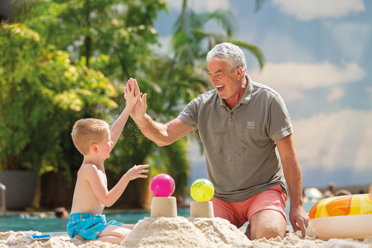 An older man and a child are playing on the beach by the South Sea and laughing as they high-five each other