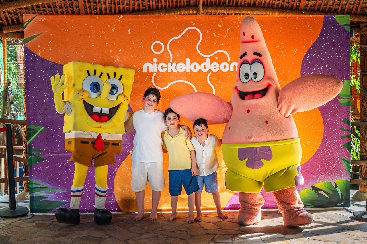 Three boys are standing next to SpongeBob and Patrick, laughing and waving.